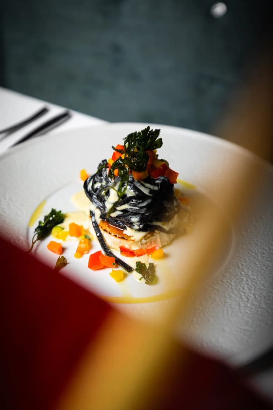 Schwarze Pasta mit Gemüse, im Vordergrund eine rote Blüte