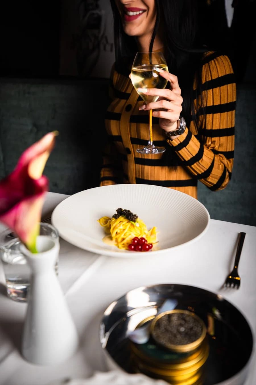 Gast mit einem Glas Weißwein, davor Pasta und Kaviar
